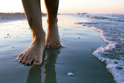 Low section of woman walking on shore at beach during sunset