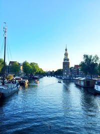 Sailboats in river by buildings against clear sky