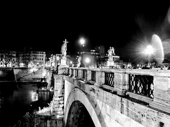 Illuminated bridge over river in city against clear sky at night