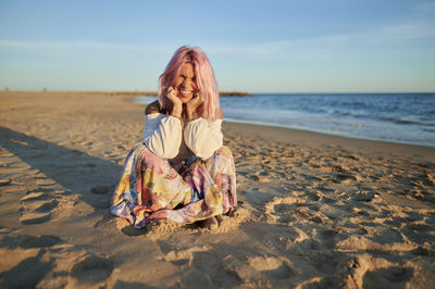 Woman sitting on shore at beach against sky