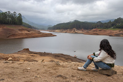 Full length of woman sitting y lake against sky