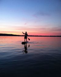 Silhouette man paddle boarding against sky during sunset