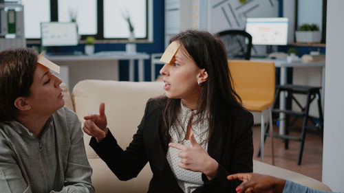 Colleagues with sticky notes on forehead talking at office