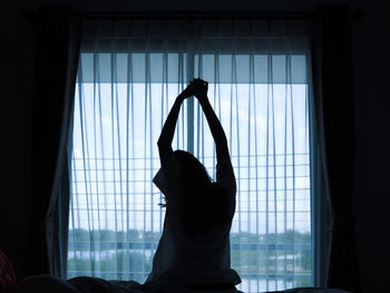 Rear view of woman stretching against window at home