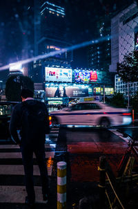 Rear view of man standing on road at night