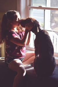 Girl with dog sitting by window at home