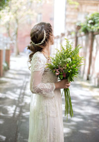 Side view of bride holding bouquet while standing on street