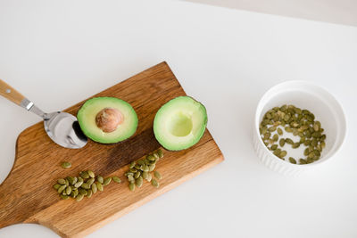 Still life sliced avocado with pumpkin seeds lies on a wooden board on a white table, top view.