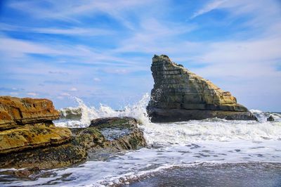 Sea waves splashing on shore against sky