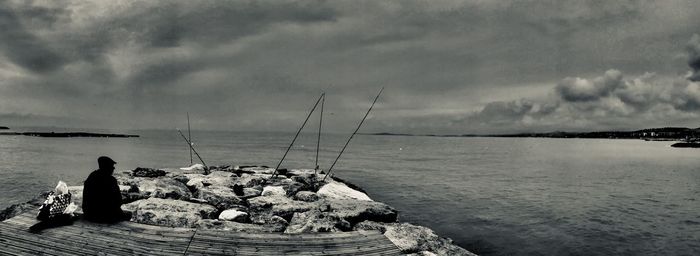 Rear view of man fishing in sea against sky