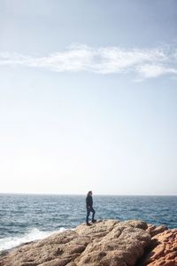 Man standing on rock looking at sea against sky