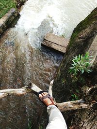 Low section of person standing on rock against waterfall in forest