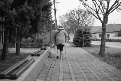 Rear view of man using crutch while walking on sidewalk