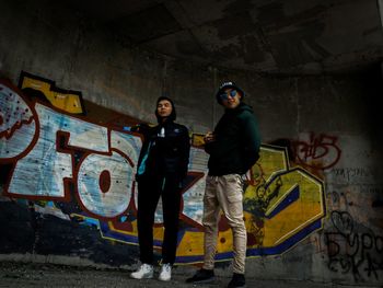 Portrait of young couple standing against graffiti wall