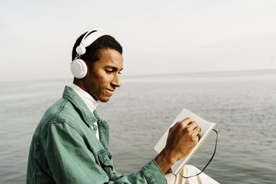 Side view of young man using mobile phone against sea