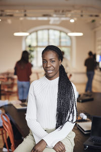 Portrait of confident female business professional with braided hair sitting at desk in office