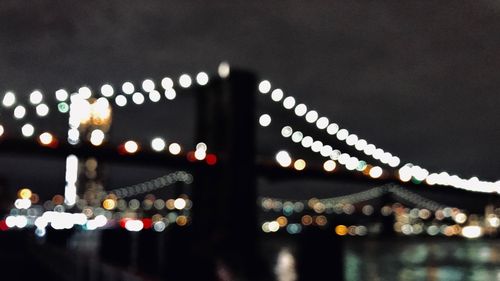 Defocused image of illuminated bridge against sky at night