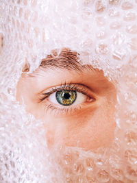 Close-up portrait of boy peeking through hole in bubble wrap