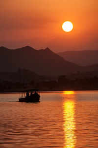 Silhouette boat in lake against orange sky