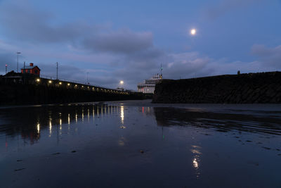 Illuminated bridge over river against sky at night