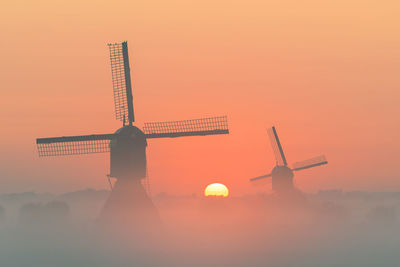 Low angle view of traditional windmill against orange sky