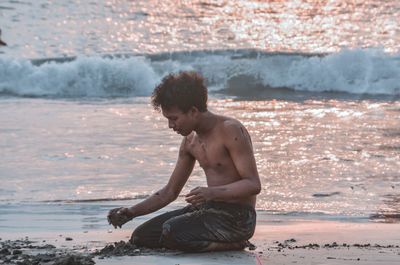Full length of shirtless man sitting at beach