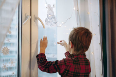 Little cute caucasian boy decorating window with christmas stickers.