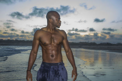 Shirtless man standing at beach against sky