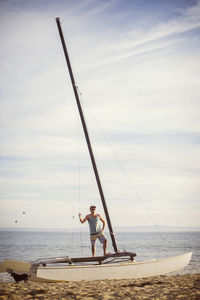 Man in sunglasses standing on sailboat at beach against sea