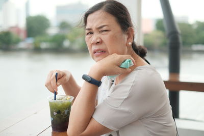 Portrait of senior woman holding drink while sitting outdoors