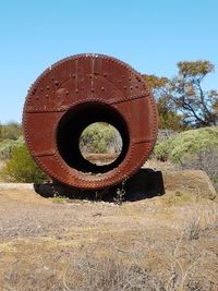 Close-up of rusty wheel on field against clear sky