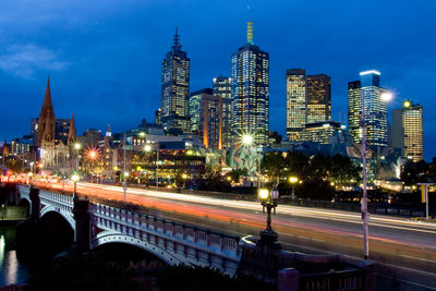 Illuminated buildings by street against sky at night