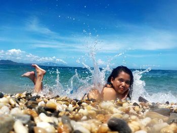 Woman splashing water at beach against blue sky