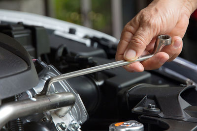 Cropped hand of mechanic repairing car engine with wrench