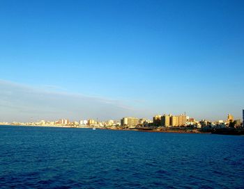 Sea by city against clear blue sky