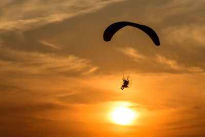 Low angle view of silhouette person paragliding against sky during sunset