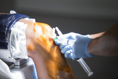 Cropped hands of doctor injecting syringe on patient knee in operating room