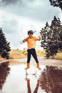 Full length of boy standing on wet glass against sky