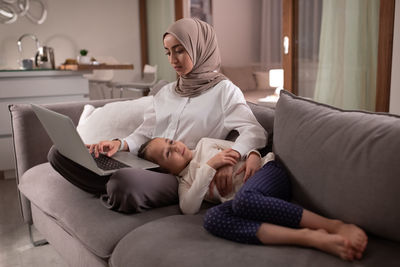 Muslim woman working remotely near girl