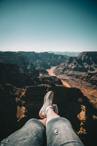 Low section of woman sitting on rock against sky