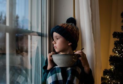 Young boy sat on a window sill with a cereal bowl looking outside