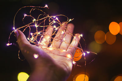Cropped hand holding illuminated string lights at night