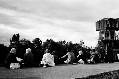 Group of people sitting on built structure against sky