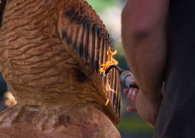 Cropped image of man using blow torch on wooden sculpture