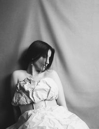 Rear view of woman sitting on bed against wall