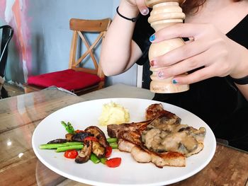 Midsection of woman using pepper mill on food while sitting at table