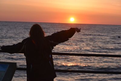 Rear view of silhouette woman standing at beach during sunset