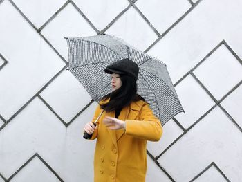 Young woman with umbrella standing against wall