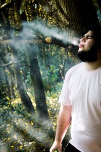 Young man looking away while standing on tree trunk in forest