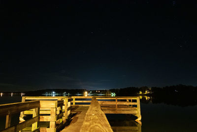 Illuminated pier over lake against sky at night
